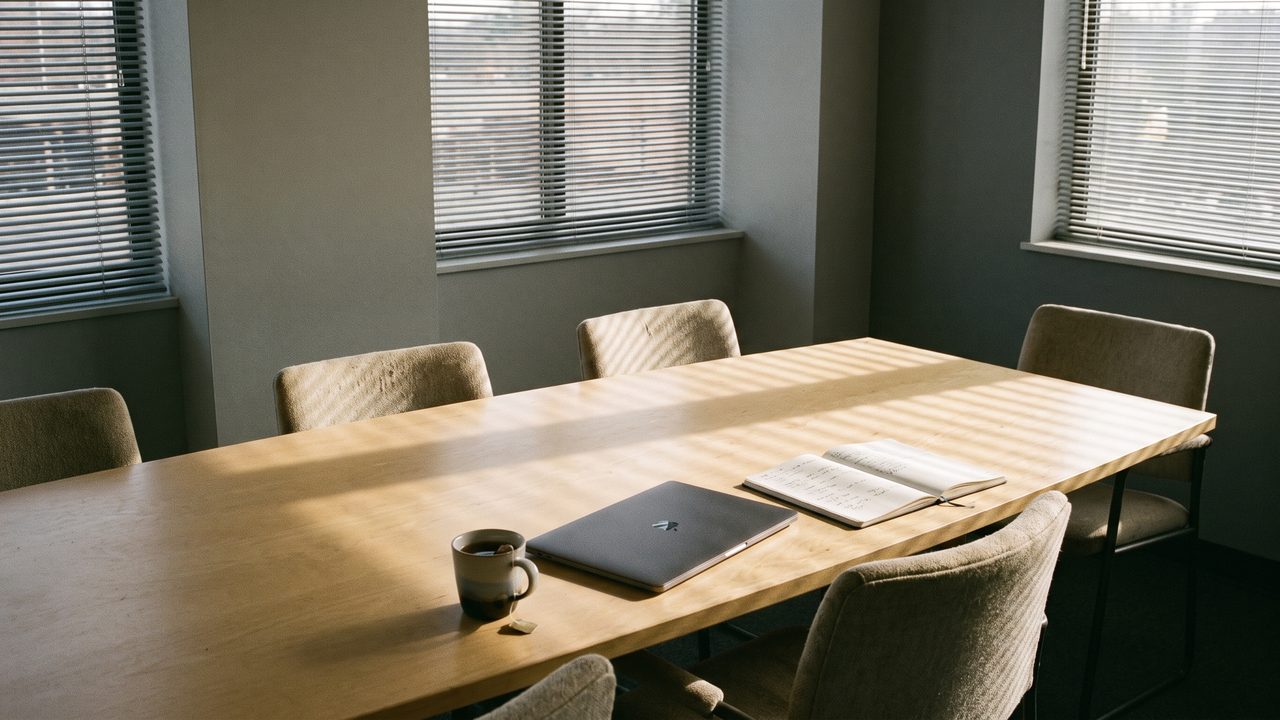 A conference room table with a closed laptop, a notebook and a cold cup of tea