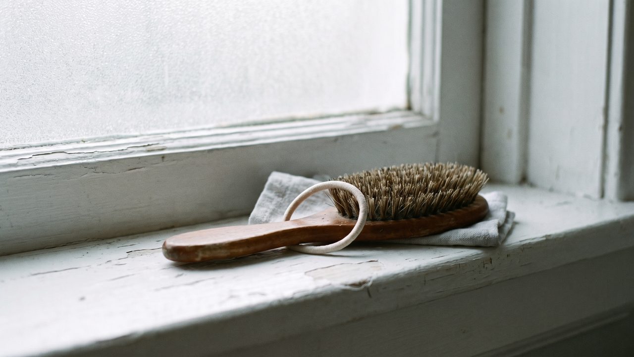 A wooden hairbrush and a hair tie on a bathroom windowsill